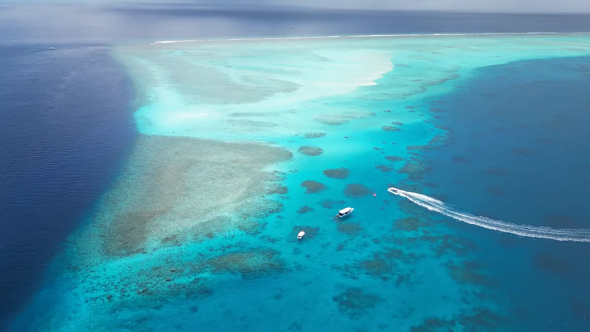 Aerial over a Maldivian reef, boats at anchor in the turquoise shallows